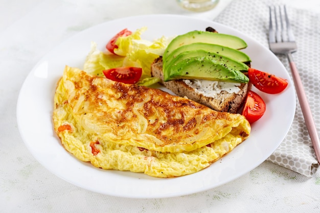 Omelette with tomatoes and toast with avocado on white plate Frittata italian omelet