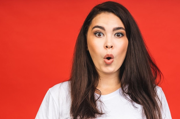 OMG Portrait of amazed shocked surprised young woman isolated over red background