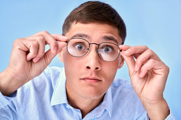 OMG Studio shot shocked caucasian man holds hands on the rim of glasses cant believe his eyes curious look at camera emotional reaction to unexpected news isolated on blue background