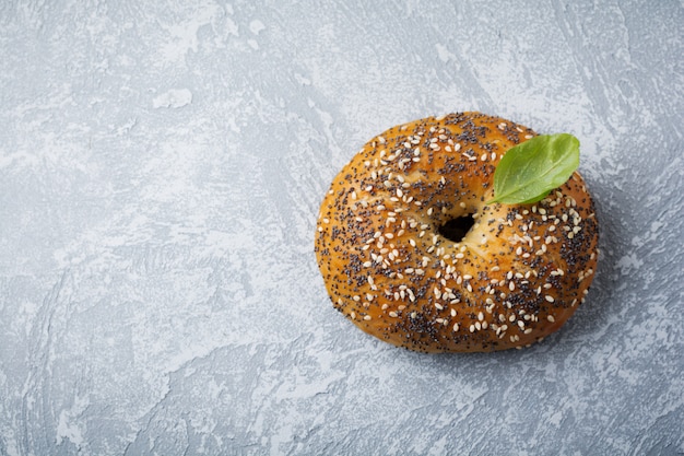 One bagel with poppy seeds and sesame seeds on a gray stone background