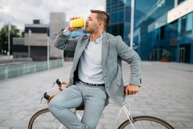 One businessman with bike drinks coffee in downtown. Business person riding on eco transport on city street