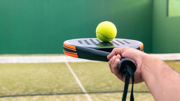 One caucasian man with the ball on top of the padel racket at green court grass