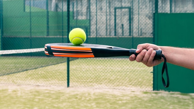 One caucasian man with the ball on top of the padel racket at green court grass