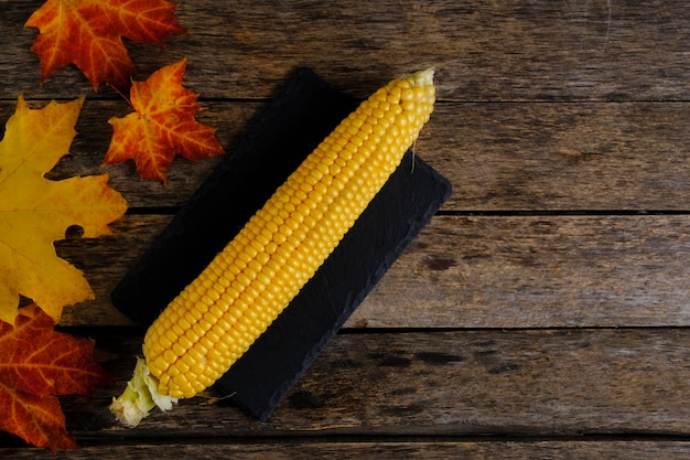 One corn on wooden chopping board and autumn maple leaves falling on table