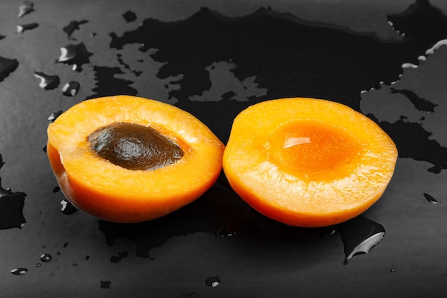 One cut apricot wet on a wet dark background Fresh juicy ruddy apricot on a dark clay plate