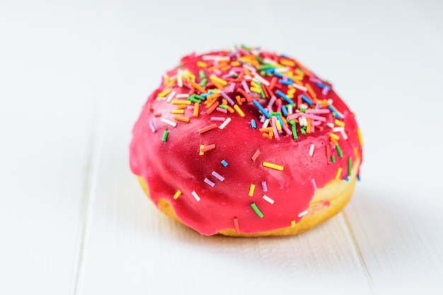 One doughnut on a white table with red frosting