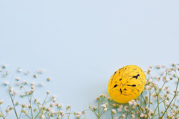 One egg is yellow with black spots and flowers on a light blue background with a copy of the space. Easter. Minimalism. Festive background. Postcard. Frame