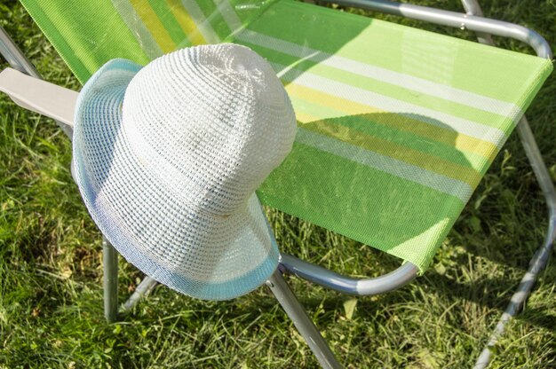 One empty folding garden chair for relaxing stands on the green grass on the lawn on a Sunny summer day a copy of the space a hat hanging on the chair