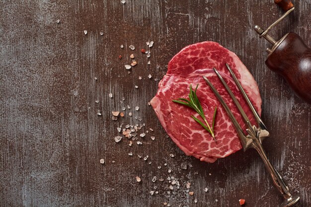 One fresh Parisienne raw steak on white parchment paper with salt, pepper and rosmary in a rustic style on old stone background. Black angus. Top view.