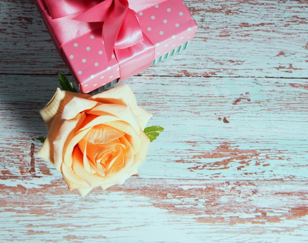 One gift box with a pink bow on a wooden background, copy of the text space one rose nearby.