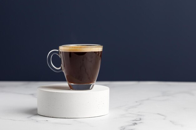 One glass coffee cup with espresso on podium and white marble background Aroma ristrettoBlue wall