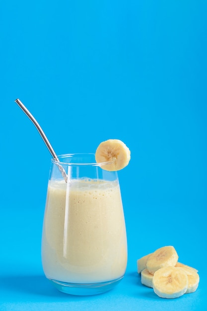 One glass of protein milkshake made of ripe sweet banana fruit blended with milk on blue background