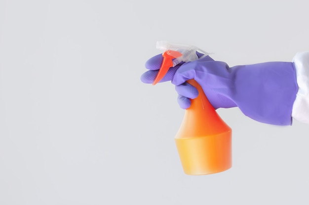 One hand in a purple rubber glove holds an orange spray bottle with cleaning agent