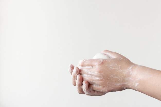 One hand on top, the other on the bottom hold the soap between the soapy palms on a white background. The concept of the need to wash hands to prevent diseases.