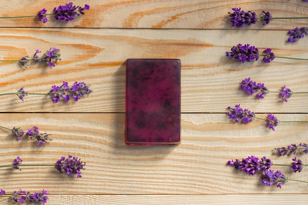 One handmade lavender soap with dried lavender flowers on wooden table surrounded with fresh lavender flowers.