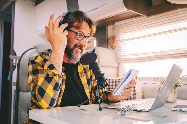 One hipster man travel and work on a camper van recording voice content for a podcast Concept of online job and smart working or digital nomad free lifestyle Male using laptop and microphone