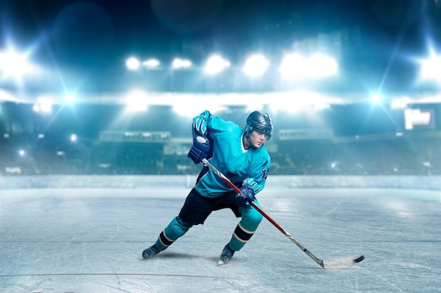 One hockey player skating with stick on ice arena, spotlights on background. Male person in helmet, gloves and uniform playing game