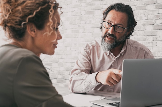 One man explain concept at work to a woman sitting at the desk Business couple at office using laptop together Lawyer and client Modern business people Back view of female and male working together