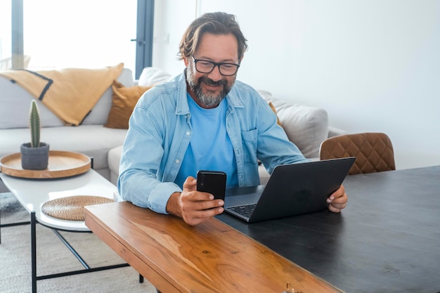 One man at home using mobile phone and laptop on the table. Concept of online small business and smart working people lifestyle. Communication with cell and computer. Technology. Modern adult people