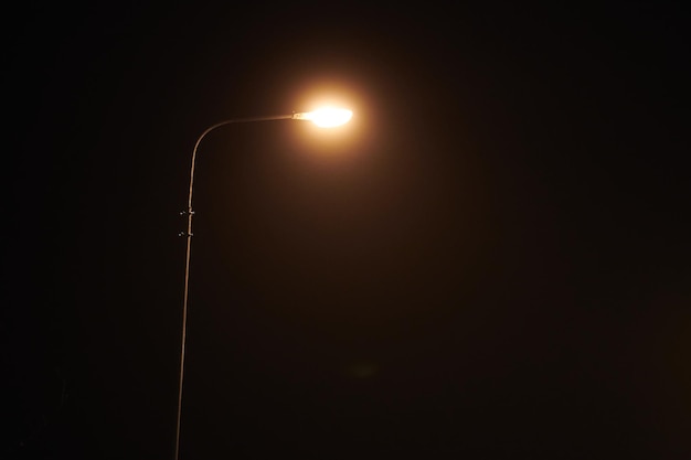 One night lamppost shines with faint mysterious yellow light through evening fog copy space