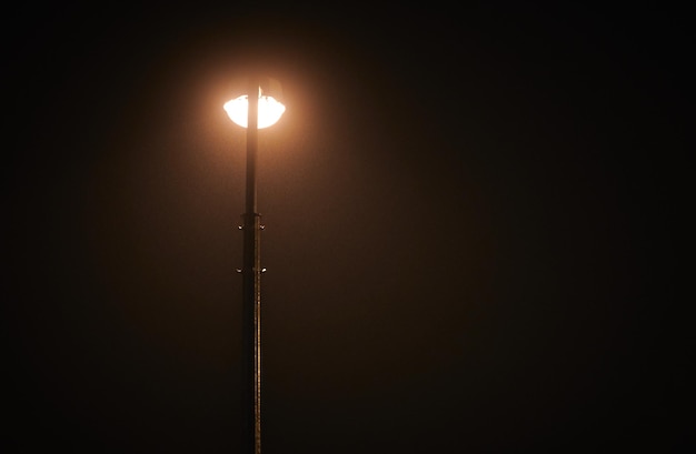 One night lamppost shines with faint mysterious yellow light through evening fog right copy space