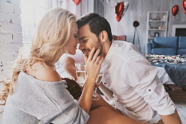 One and only. Beautiful young couple drinking champagne and smiling while sitting face to face in the bedroom