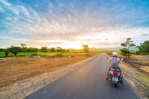 One person on motorbike looking at view mountains in the Phu Yen province, Nha Trang Quy Nhon, adventure traveling in Vietnam. Rear view sunburst dramatic sky at sunset.