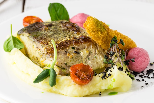 One piece of baked salmon grilled pepper lemon and salt on a brown plate with lettuce leaves. wood surface