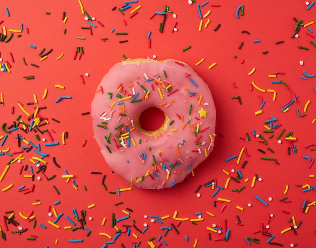 One pink round donut with colored sprinkles on a red background