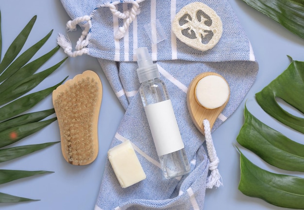 One pump dispenser on blue bath towel near tropical leaves and skin care accessories mockup