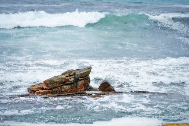 One rock with waves crashing around it Rock formation in calm peaceful blue ocean Waves moving in and out by the seaside Rocky shoreline with clear water Holiday location for travel destination