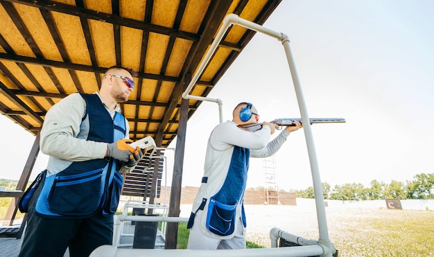 One shooter holds a remote control for launching targets and the second shooter aims at them