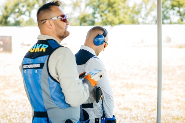 One shooter holds a remote control for launching targets and the second shooter aims at them