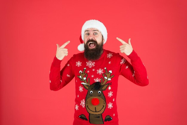 One Stop Shopping. christmas time. male at xmas party. happy new 2020 year. funny hipster sweater. knitwear fashion. winter holiday celebration. feel joy and hapiness. bearded man santa hat red wall.