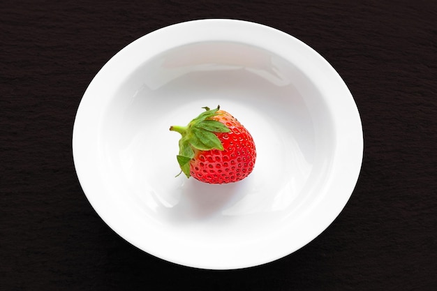 One strawberry Strawberries in a white plate on a black background Healthy berries Natural organic food