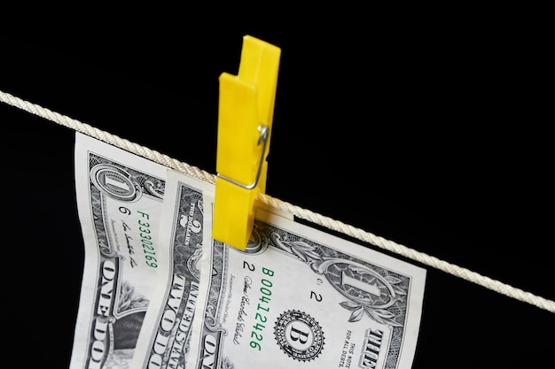 One and two dollar banknotes fastened with clothespins are dried on a clothesline on a dark background