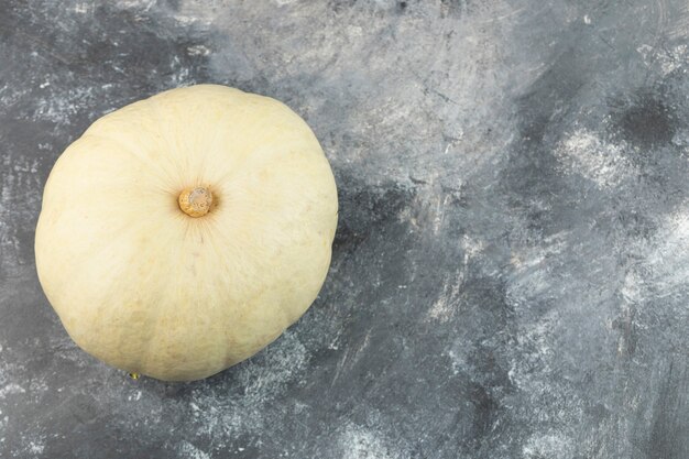 One whole fresh grey pumpkin placed on a marble table . 