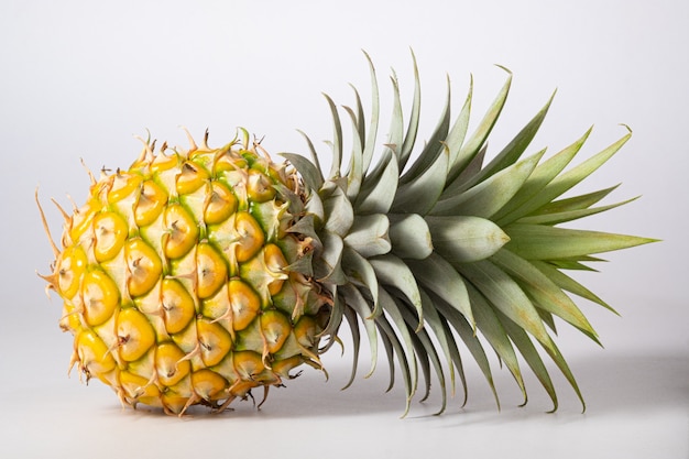 One whole pineapple with green leaves on white wall. Ripe pineapple is yellow.