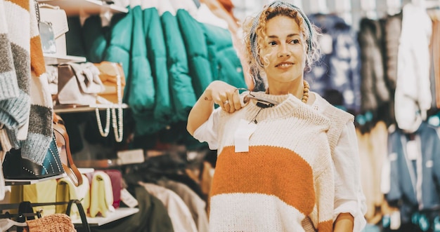 One woman doing shopping activity inside a garment clothes store smiling and looking sweaters Sales holiday discount season on commercial centre Female people and fashion trendy business Happy lady