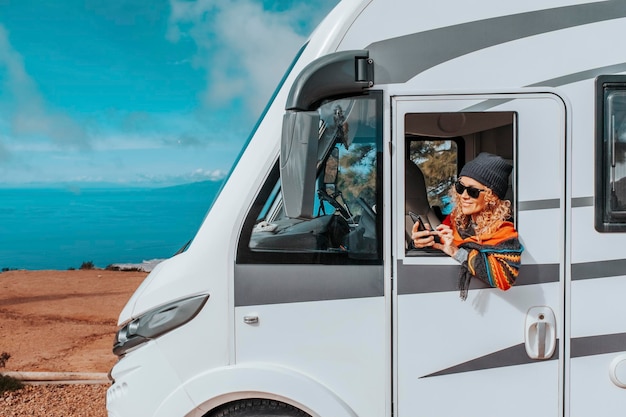 Photo one woman enjoy arrival vacation travel destination after drive a big camper van motor home concept of happy female people in van life lifestyle summer journey planning road trip on mobile phone