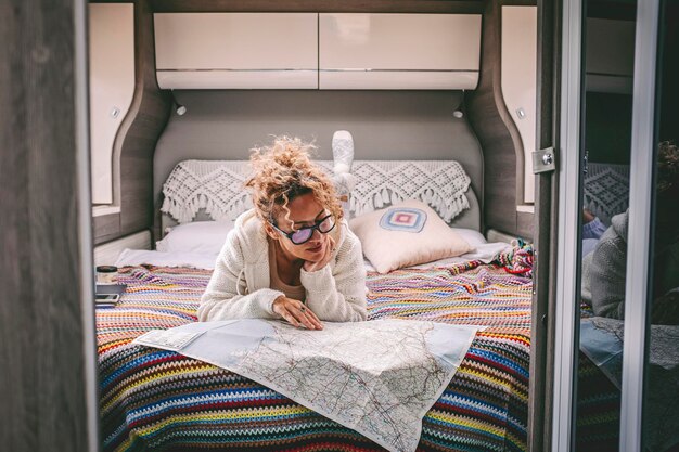 Photo one woman planning next travel trip destination laying in bed inside a mpodern camper van motorhome people and vanlife lifestyle traveler female looking paper map guide for road map indoor leisure