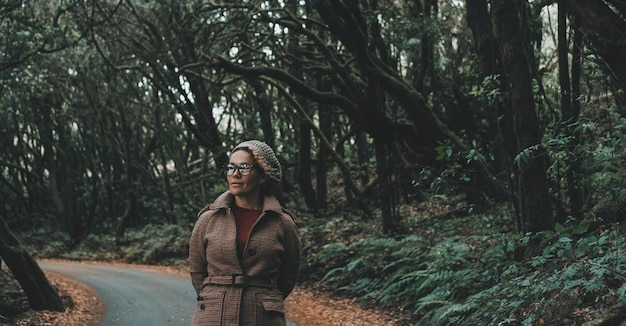 One woman walking in the green forest woods on road with trees around enjoying nature and environment national park Winter outdoor leisure activity with female people tourist enjoying scenic place