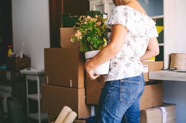 One woman with plant inside new flat apartment after home moving activity People changing home concept work Young female inside new property renting with carton box cardboards in background