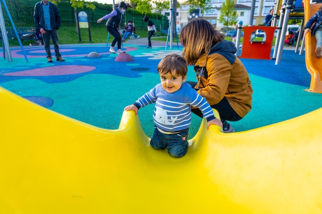 One year old Caucasian boy playing swings with his mother playing in the park jumping on a yellow squeaker