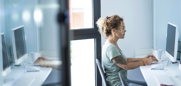 One young modern woman working on computer sitting at the desk in office bright corporate workplace Tattoo Professional new normal entrepreneur home work lifestyle Mirrored and copy space concept