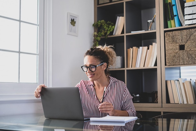 One young woman working at home in the office with laptop and notebook taking notes talking in a video conference One businesswoman calling communicatingxA