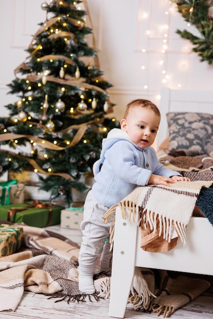 A oneyearold boy sits near a decorated Christmas tree with gifts Christmas tree in the house A happy child is waiting for the new year