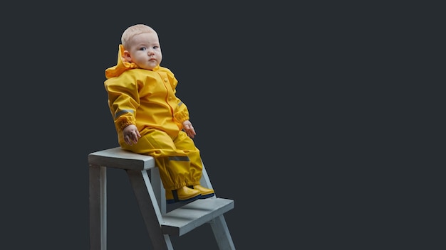 Oneyearold boy sitting on stairs in yellow waterproof suit