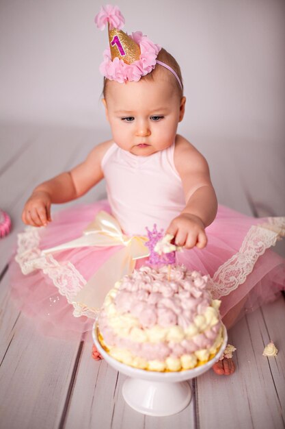 Oneyearold little girl with her first birthday cake trying sugar and celebrating birthday