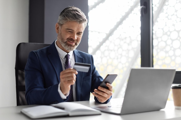 Online Banking Middle Aged Businessman Using Smartphone And Credit Card In Office